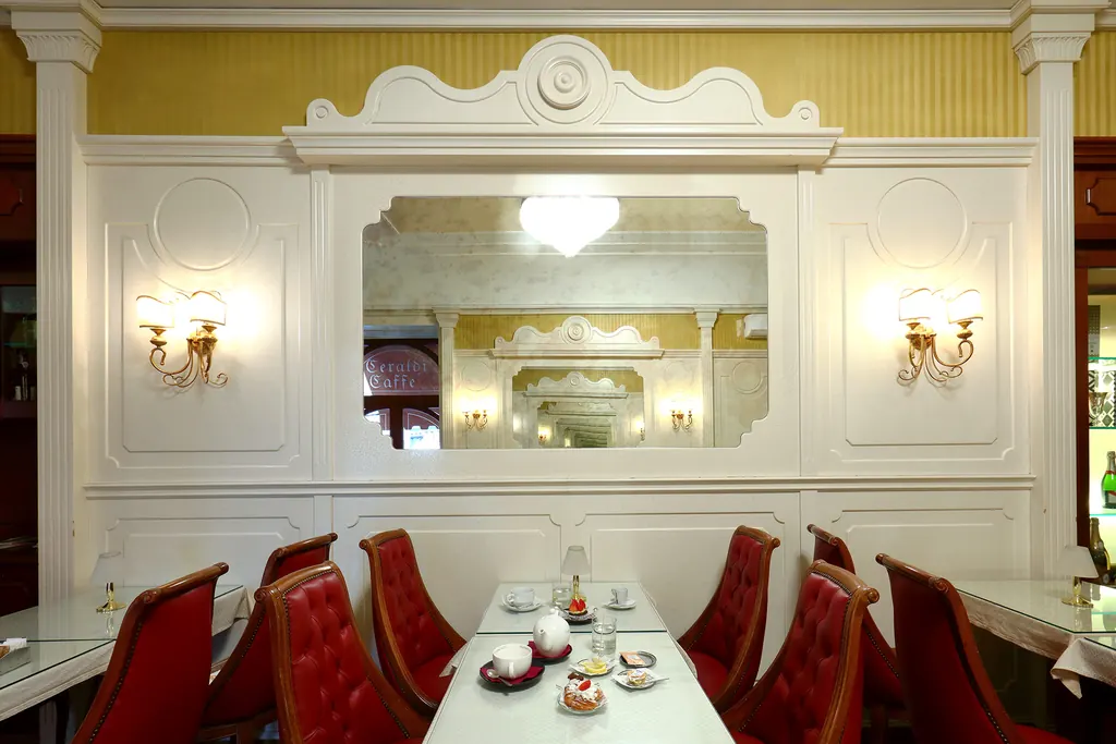 La sala bianca e oro di Ceraldi Caffè con i tavolini e le poltroncine rosse